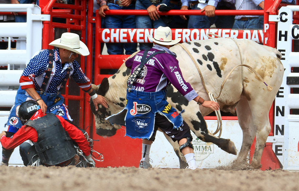 Dos payasos de rodeo y un jinete apartándose del camino de un toro.